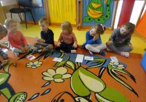 Dzieci siedzą przed ułożonymi obrazkami szczoteczek do zębów, kubków i pasty do zębów.